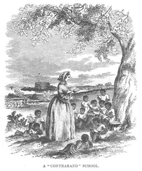 A group of children sit under a tree, a teacher standing in front
of them. A fort can be seen in the background.