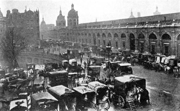DELIVERING MEAT AT SMITHFIELD TODAY

There is an inclined road by the tree in the center of the picture, leading
to the special railroad freight depot. Cars are also run directly under the
market and their cargoes are delivered by hydraulic lifts to the stands above.